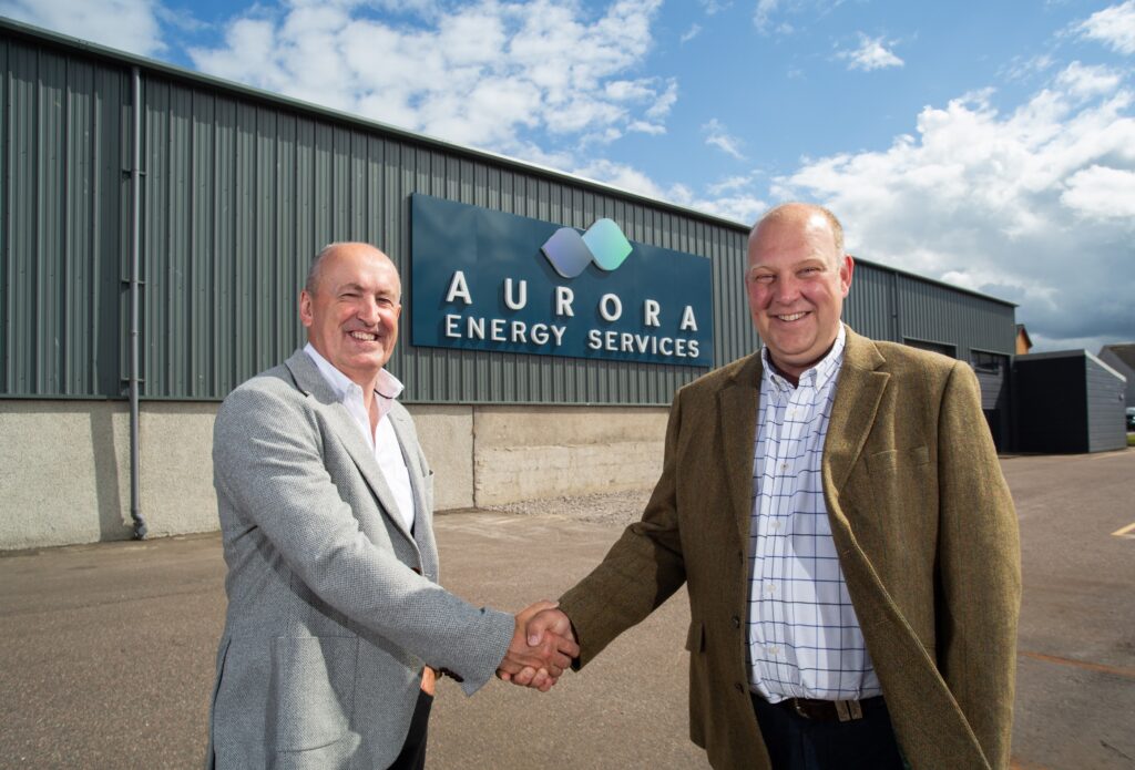 Two smiling, smartly dressed men, Doug Duguid and Alasdair Noble shake hands outside an industrial style building signed 'Aurora Energy Services'